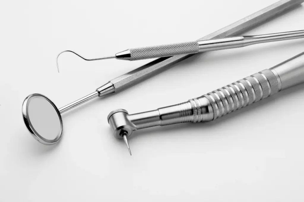 A dental mirror, probe and handpiece laid out on a clean surface