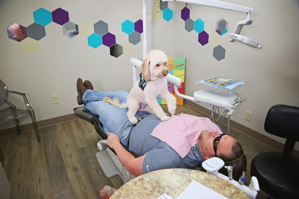 A patient in the chair with a therapy dog in a treatment room at Diamond Dental in Tulsa